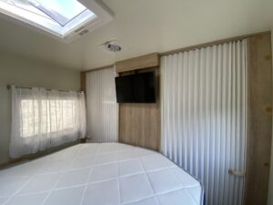 Chambre lumineuse avec lit, fenêtre, TV et rideaux blancs.