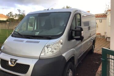 Camping-car gris garé devant une maison.