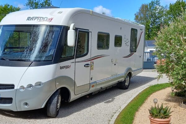 Wohnmobil weiß Rapido neben Bäumen geparkt.