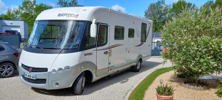 Camping-car blanc Rapido stationné à côté d'arbres.