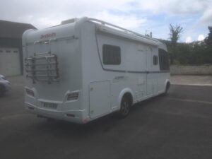 Camping-car blanc stationné devant des bâtiments.