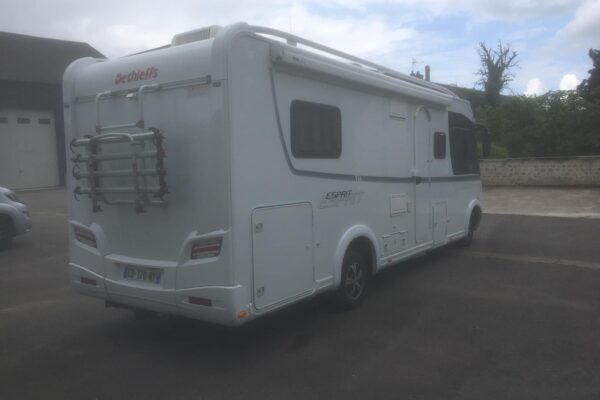 Camping-car blanc stationné devant des bâtiments.