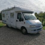 Camping-car blanc stationné dans jardin verdoyant.
