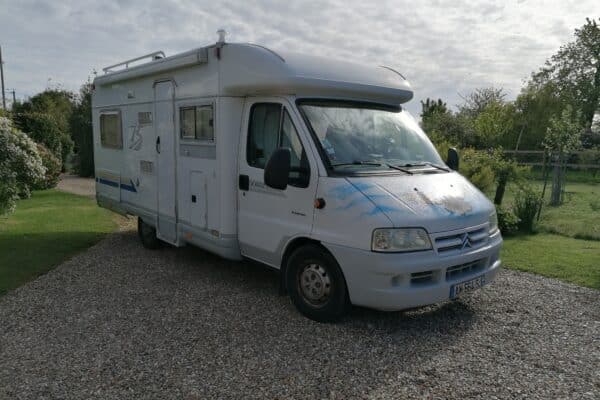 Camping-car blanc stationné dans jardin verdoyant.