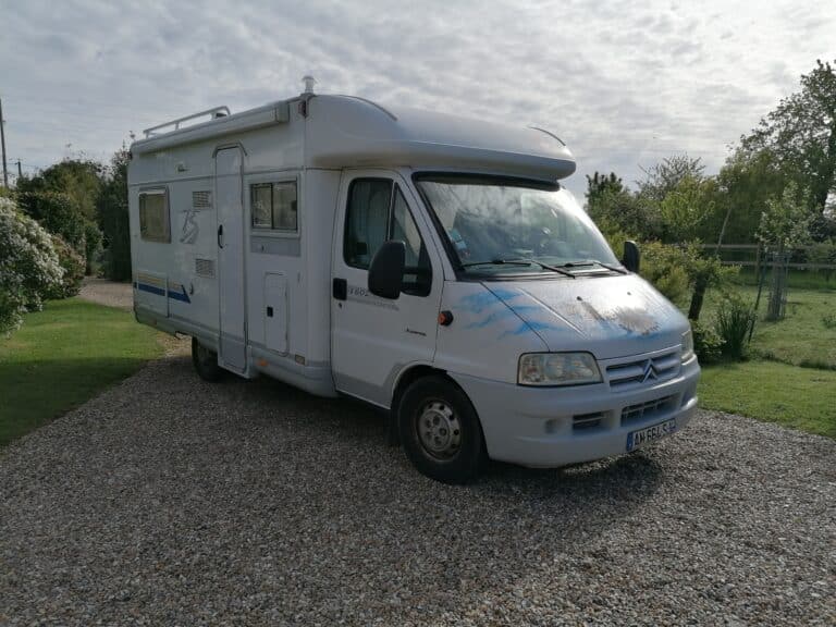 Camping-car blanc stationné dans jardin verdoyant.
