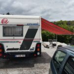 Camping-car avec auvent déployé et chien.