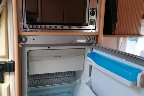 Réfrigérateur ouvert avec micro-ondes intégré en camping-car.