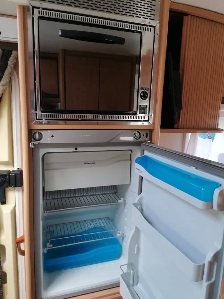 Réfrigérateur ouvert avec micro-ondes intégré en camping-car.