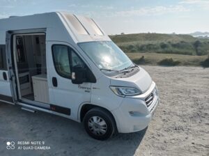 Camping-car blanc stationné sur un terrain sablonneux.