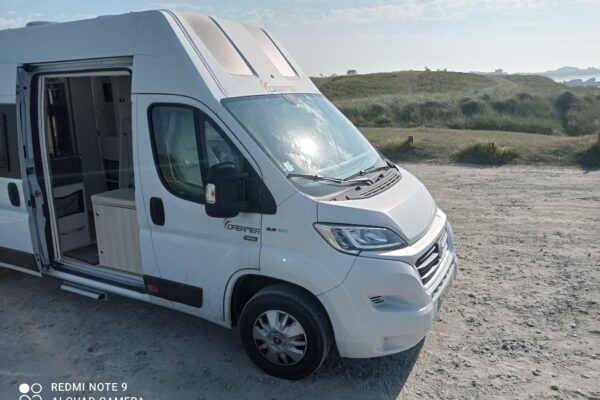 Camping-car blanc stationné sur un terrain sablonneux.