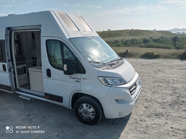 Camping-car blanc stationné sur un terrain sablonneux.
