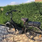 Vélo électrique noir garé devant une haie verte.