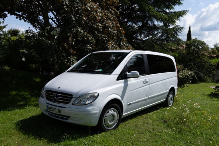 Fourgonnette Mercedes blanche stationnée dans un jardin vert.