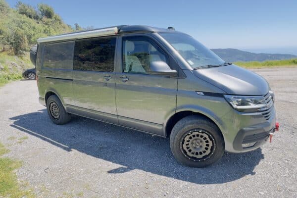 1TP272Grüner Lieferwagen in den Bergen geparkt, klarer Himmel.