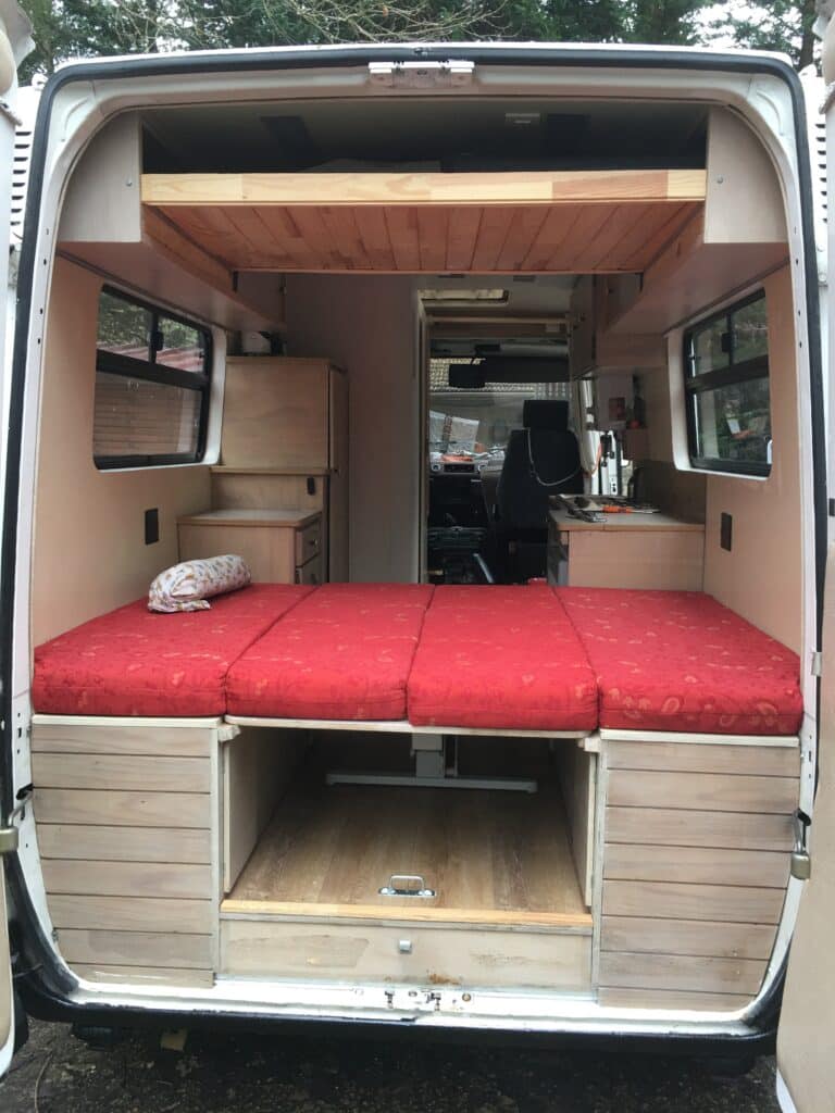 Intérieur de fourgonnette aménagée avec lit rouge.
