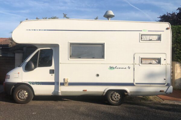 Camping-car blanc stationné, ciel dégagé.
