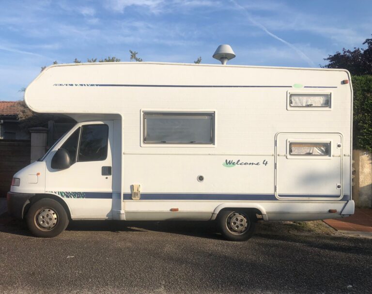 Camping-car blanc stationné, ciel dégagé.