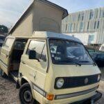 Fourgon VW beige avec toit relevable, parking.
