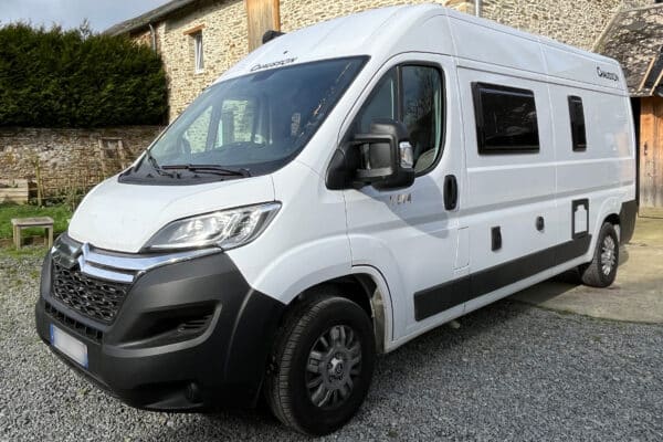 Camping-car moderne blanc stationné devant maison en pierre