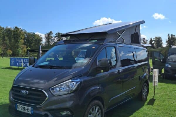 Fourgon aménagé Ford sur herbe verte, ciel bleu