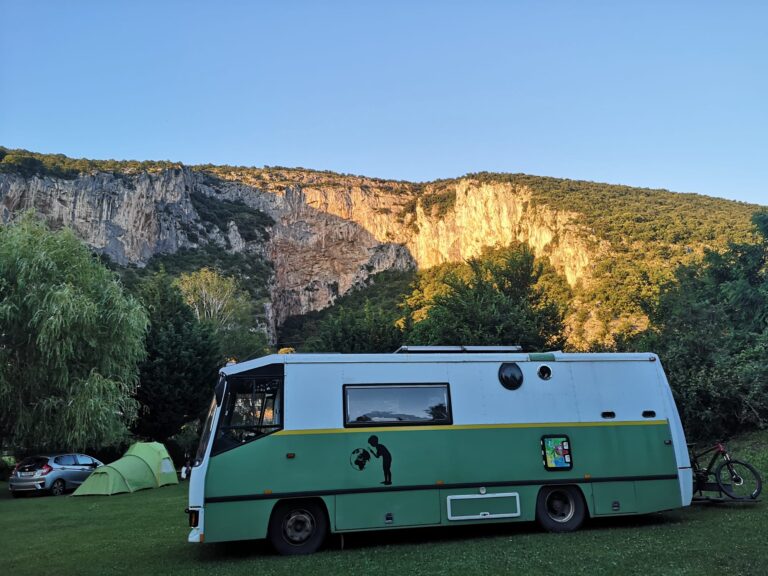Camping-car vert garé devant falaises rocheuses