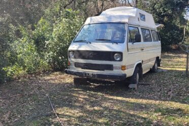 Camping-car Volkswagen blanc dans un jardin ensoleillé