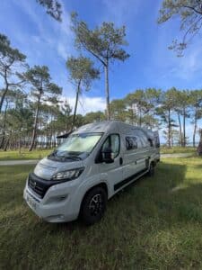 Camping-car blanc en forêt sous ciel bleu