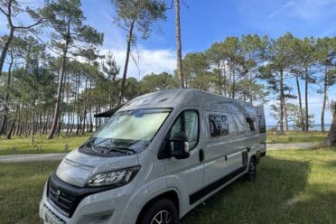 Camping-car blanc en forêt sous ciel bleu