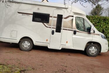 Camping-car blanc stationné devant une haie verte