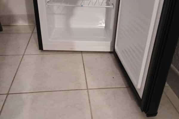 Piccolo frigorifero aperto su pavimento piastrellato beige