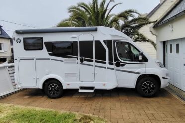Camping-car blanc garé devant maison avec palmier