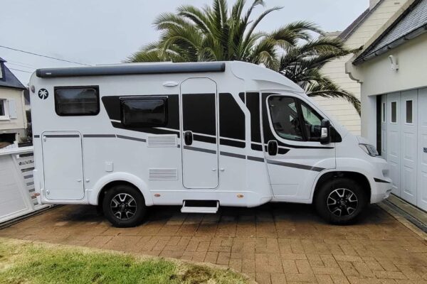 Camping-car blanc garé devant maison avec palmier