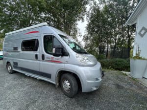 Camping-car gris devant des arbres.
