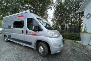 Camping-car gris devant des arbres.