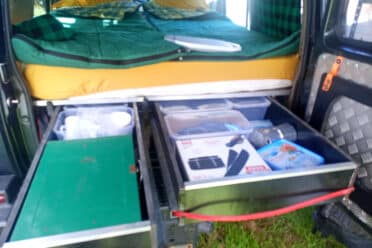 Aménagement camping-car avec lit et rangements ouverts.