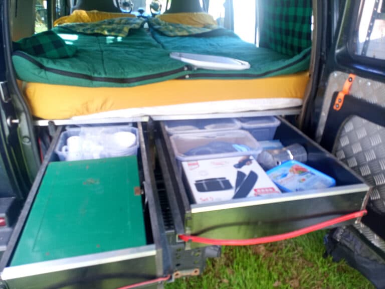 Aménagement camping-car avec lit et rangements ouverts.