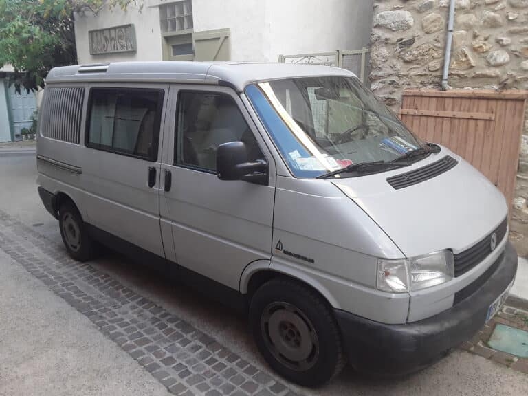 Fourgon gris garé sur une rue pavée.