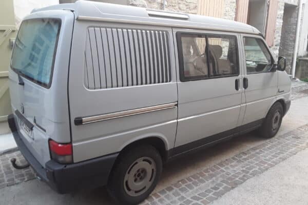 Fourgon gris stationné dans une ruelle pavée.