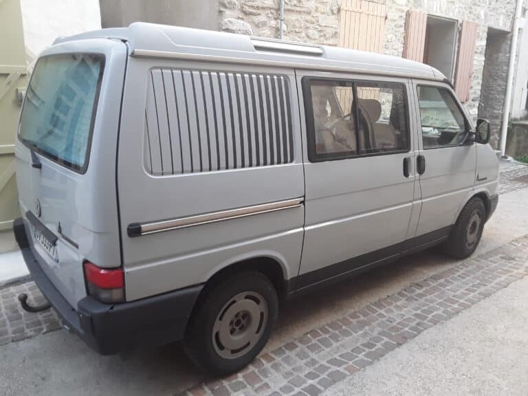 Fourgon gris stationné dans une ruelle pavée.