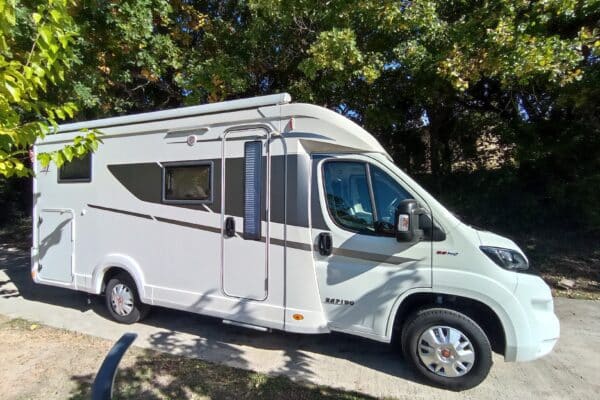 Camping-car blanc stationné sous les arbres verts