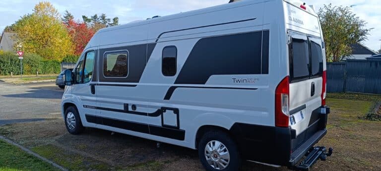 Camping-car blanc garé sur une allée résidentielle.