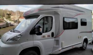 Camping-car blanc stationné près d'une maison