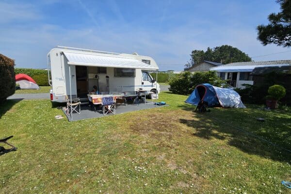 Wohnmobil und Zelt auf sonnigem Campinggelände.