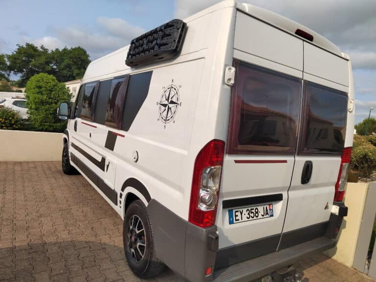 Camping-car blanc stationné sur allée pavée.