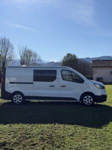 Camionnette blanche garée sur l'herbe devant montagnes.
