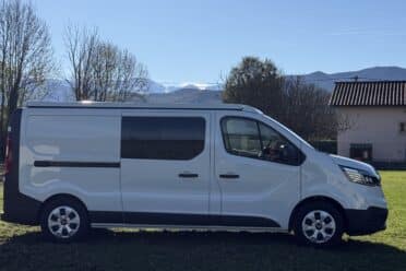 Camionnette blanche garée sur l'herbe devant montagnes.