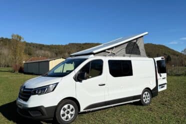 Camionnette blanche avec toit relevé sur pelouse verte.