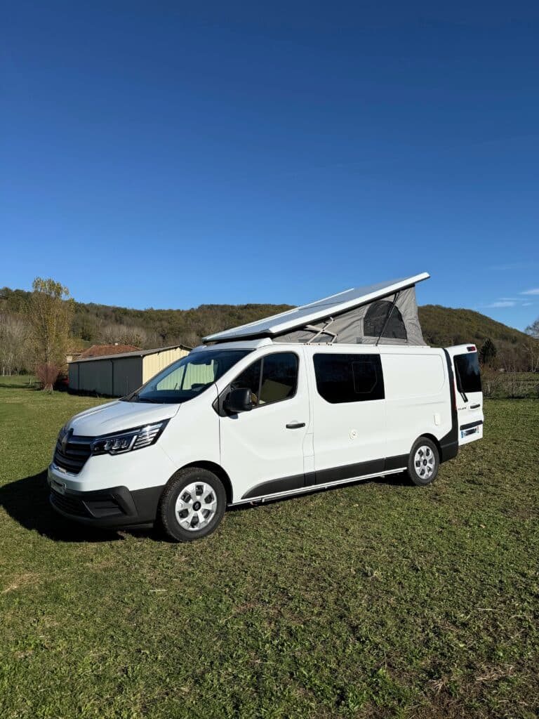 Camionnette blanche avec toit relevé sur pelouse verte.