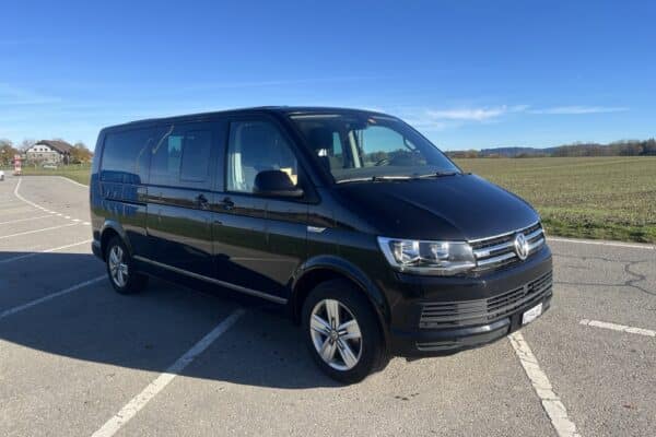 Fourgon noir garé sur une route ensoleillée.