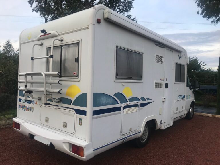Camping-car blanc garé sur allée en terre rouge.